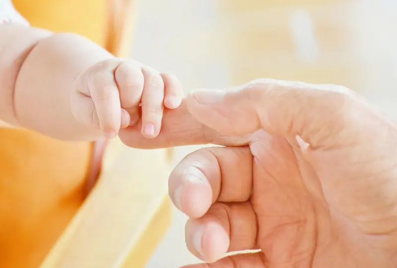 A baby holding an adult's finger