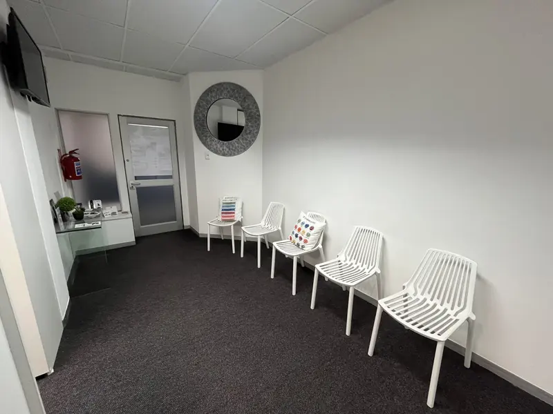 The waiting area with white chairs and a round mirror